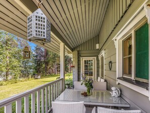 A covered porch with a glass table and wicker chairs, overlooking a grassy yard with trees. - Kiviniemi by Interhome (Punkaharju)