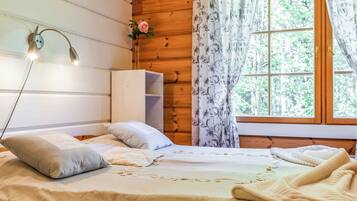 Une chambre à coucher dans une cabane en bois, avec un lit, des oreillers, une table de chevet, une lampe et une fenêtre avec des rideaux.
