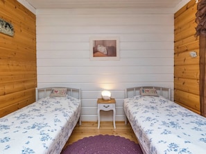 A room with two single beds, a small bedside table with a lamp, a wooden headboard, and a framed picture on the wall.