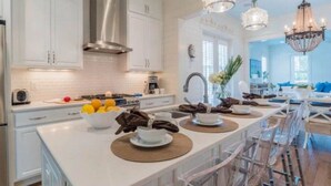 A modern kitchen with white cabinetry, a stainless steel range hood, and a dining area with a long table and chairs. - WaterColor-Santa Rosa.  Golf Cart, 2 min from beach, Community Pools (Santa Rosa Beach)