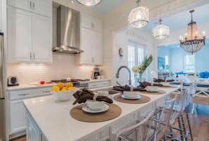 A modern kitchen with white cabinetry, a stainless steel range hood, and a breakfast bar with a bowl of fruit and coffee cups. - WaterColor-Santa Rosa.  Golf Cart, 2 min from beach, Community Pools (Santa Rosa Beach)