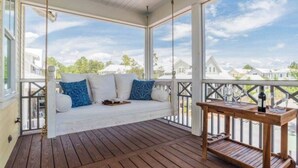 A covered porch with a swing seat, a wooden table with glasses, and a view of houses. - WaterColor-Santa Rosa.  Golf Cart, 2 min from beach, Community Pools (Santa Rosa Beach)