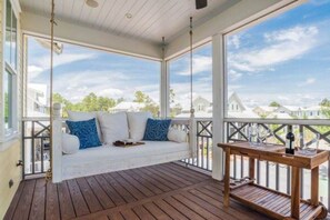 A covered porch with a swing seat and a table with glasses and a bottle. - WaterColor-Santa Rosa.  Golf Cart, 2 min from beach, Community Pools (Santa Rosa Beach)