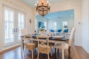 A dining area with a chandelier, white walls, and a view into a living room with a sofa and a TV. - WaterColor-Santa Rosa.  Golf Cart, 2 min from beach, Community Pools (Santa Rosa Beach)