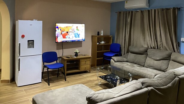 A living room with a sofa, two chairs, a TV, a refrigerator, and a wooden cabinet.