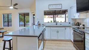 Una cocina moderna con armarios blancos, una isla grande, un ventilador de techo y una ventana con vistas a un patio trasero.