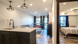 Uma cozinha moderna com ilha central, sala de jantar com cadeiras vermelhas e um quarto com cama grande e vista para o exterior.