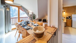 Ein gemütlicher Essbereich mit Holztisch, gedeckt für vier Personen, einem Korbwäscher und Blick auf die verschneite Landschaft durch ein großes Fenster.