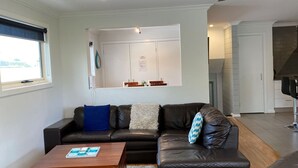 A modern living room with a leather sofa, a wooden coffee table, and a view of a kitchen and dining area.