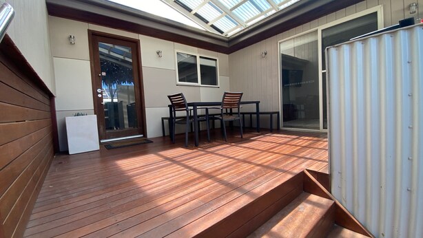 A sunlit patio with a wooden deck, a sliding glass door, and a table with chairs.