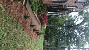 A brick building with a pathway leading to a red flower bed and green shrubs. - Welcome Home!! (Marietta)