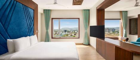A hotel room with a large bed, a desk, a television, and a view of a cityscape.