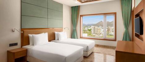 A hotel room with two beds, a ceiling fan, a large window with a view, and a TV on the right.