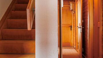 Un escalier en bois mène à un couloir doté de portes en bois et dont le sol est recouvert d’une moquette.