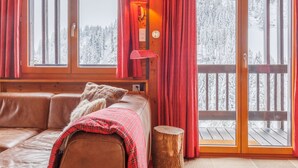 Een gezellig houten kamer met grote ramen, een rode lamp en uitzicht op een besneeuwd bos.