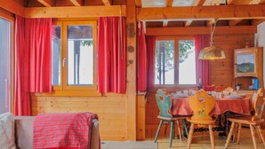 Een gezellig chaletinterieur met een houten plafond, een eethoek met een tafel voor vier personen en een bank met een geruite plaid.
