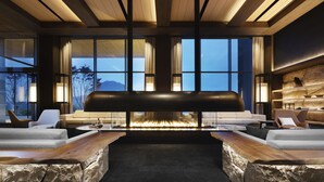 Un área de descanso moderna con chimenea de piedra, asientos cómodos y ventanas amplias con vistas al exterior.