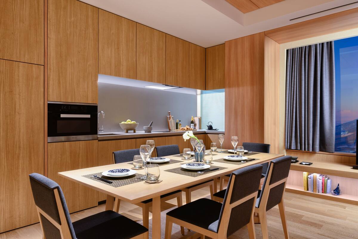 A modern kitchen with wooden cabinetry, a built-in oven, and a dining area with a table set for four.