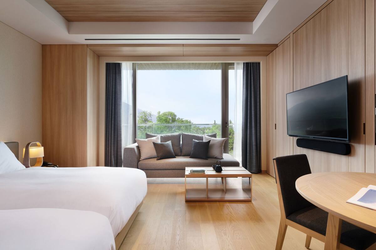 A hotel room with a bed, a sofa, a coffee table, a TV, and a view of the outdoors.