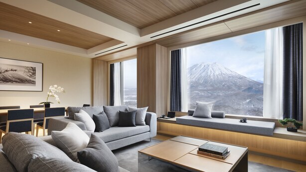 Una sala de estar moderna con sofá, mesa de centro y vistas a la montaña a través de amplios ventanales.