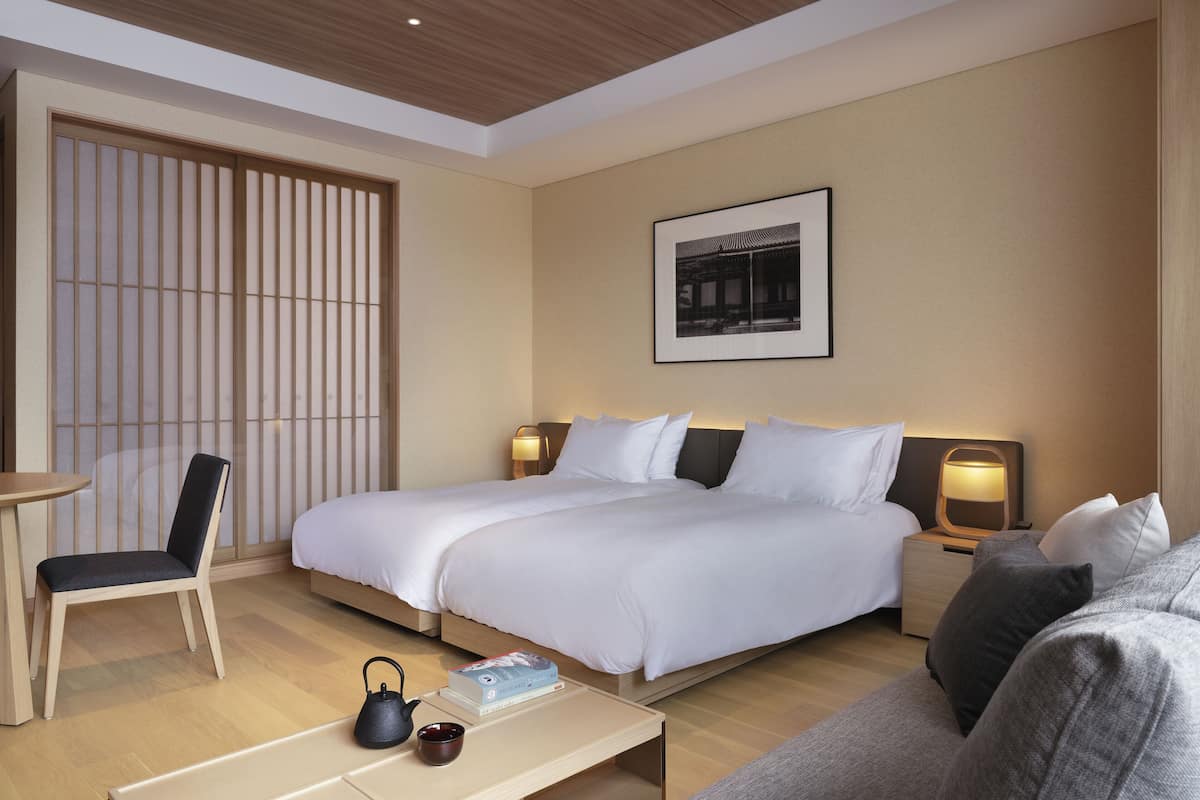 A hotel room with a bed, bedside tables, a chair, a coffee table, and a picture on the wall.