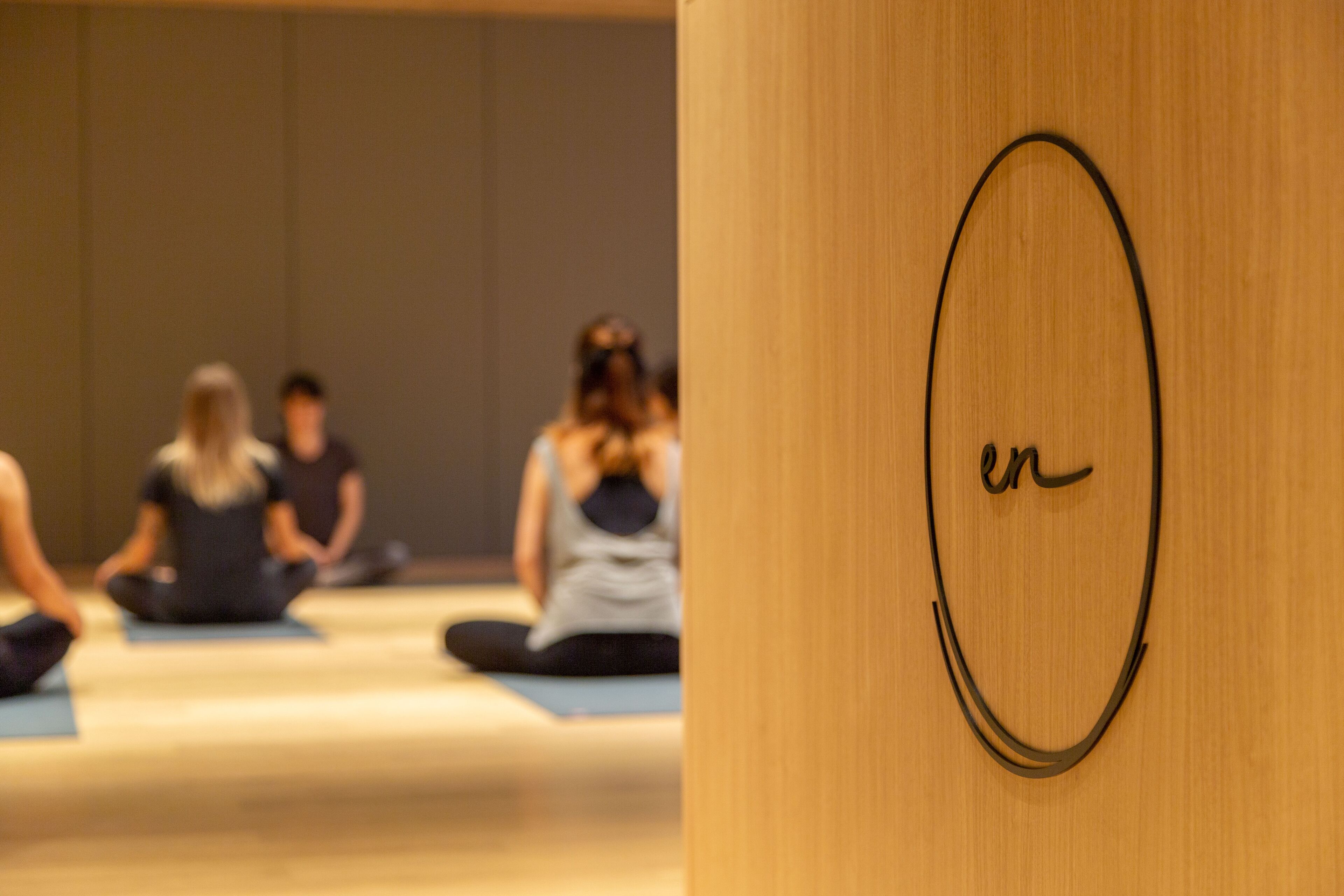 Clase de yoga borrosa en una habitación con pared de madera y un diseño circular.