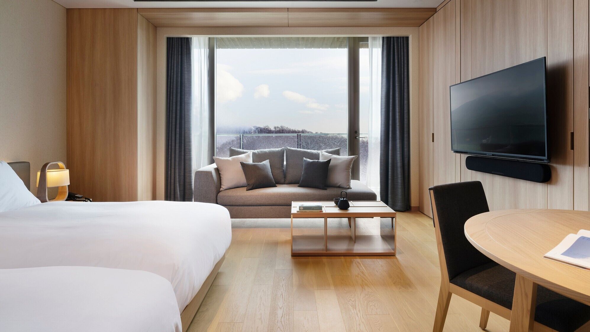 A hotel room with a bed, a sofa, a coffee table, a TV, and a view of the outdoors.