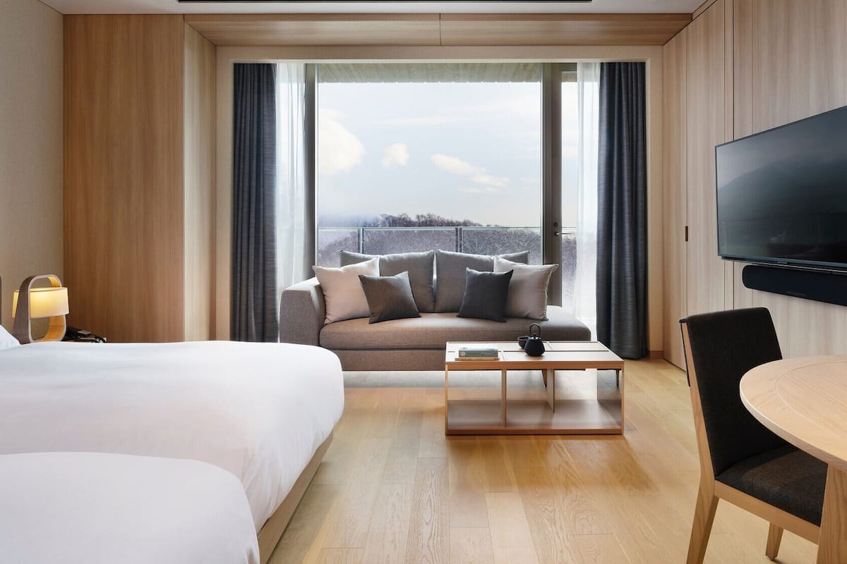 Una camera d'albergo con un letto, un divano, un tavolino da caffè, una TV e vista sull'esterno.