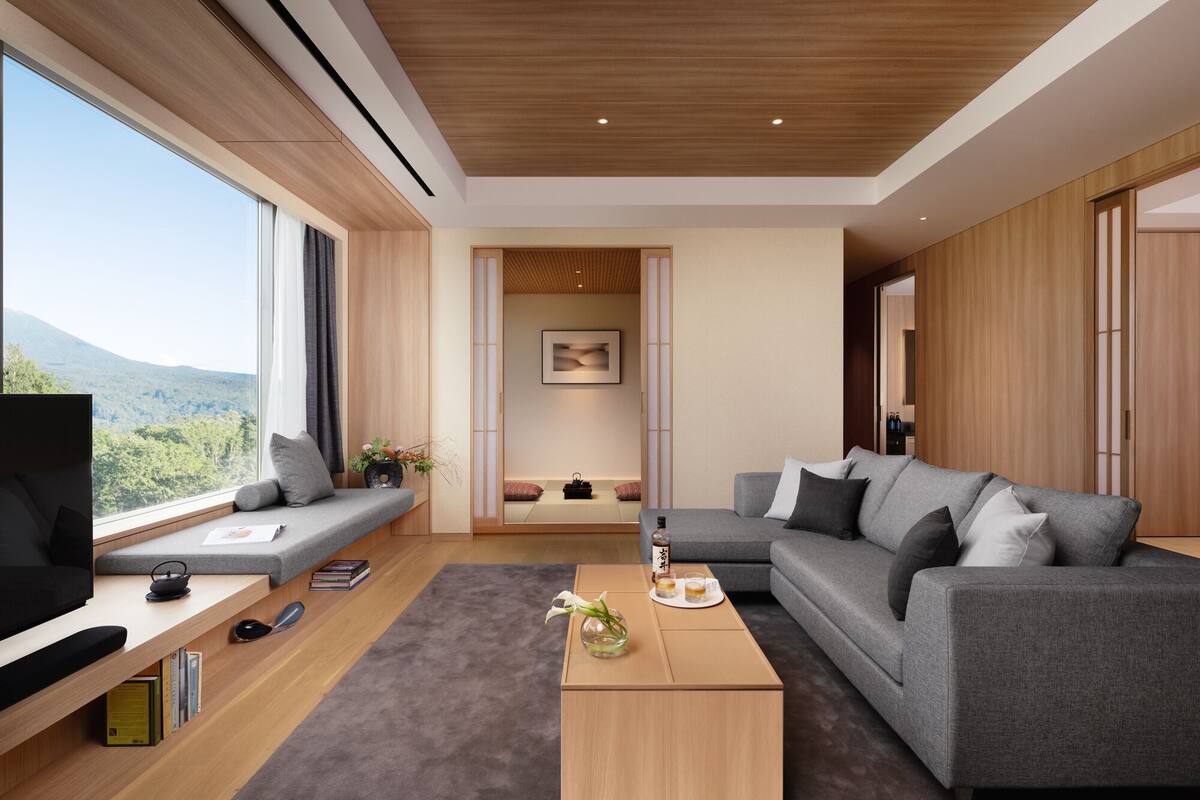 A modern living room with a large window, a grey sofa, a coffee table, and a TV.