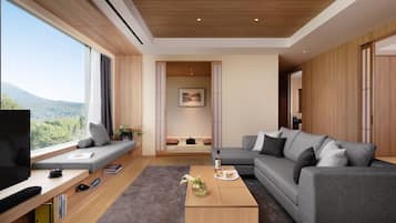A modern living room with a large window, a grey sofa, a coffee table, and a TV.