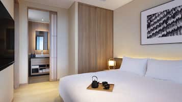 A hotel room with a large bed, a bedside table with a lamp, a wooden side table with a tray of tea, a wardrobe, and a framed picture on the wall.