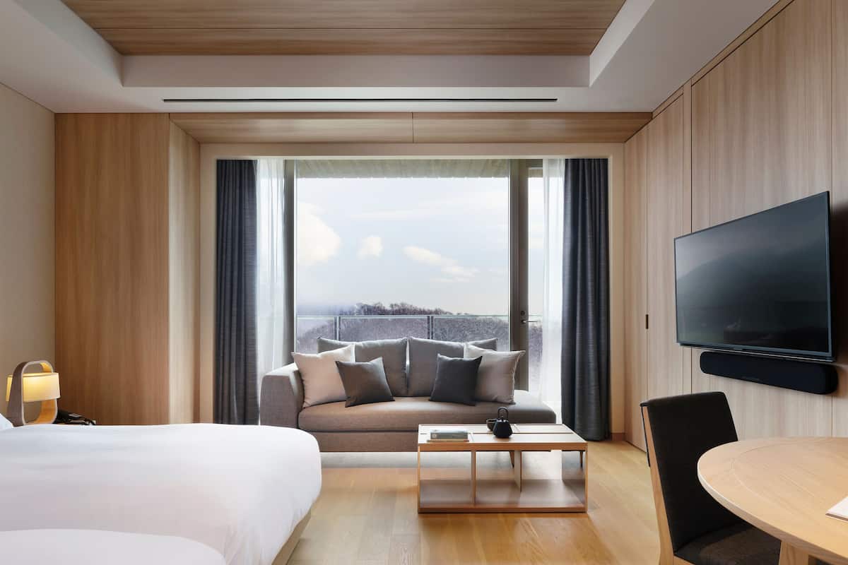 A hotel room with a large bed, a sofa, a coffee table, a TV, and a balcony with a view.