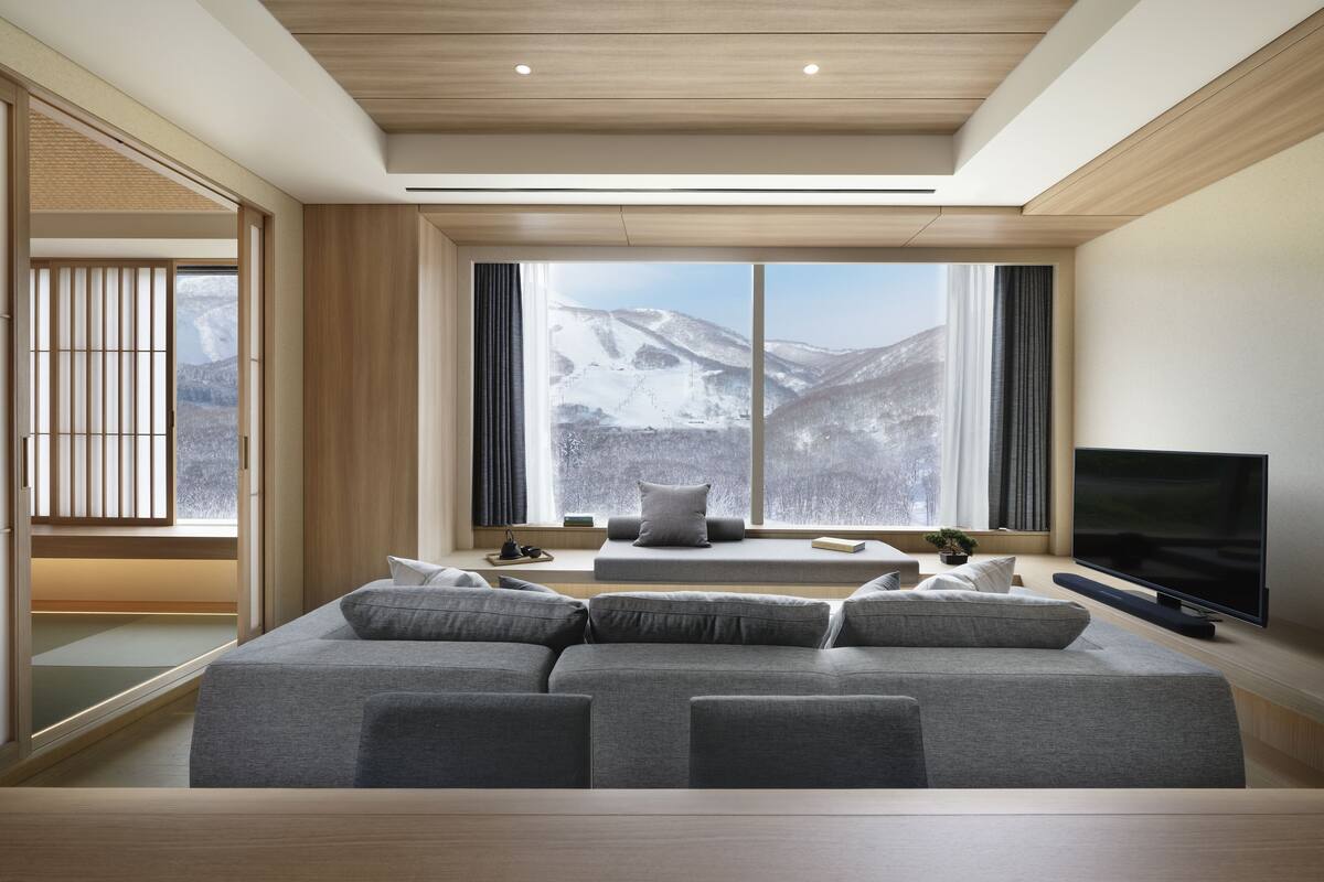 A modern living room with a large window, a sofa, a flat-screen TV, and a small table with a plant.