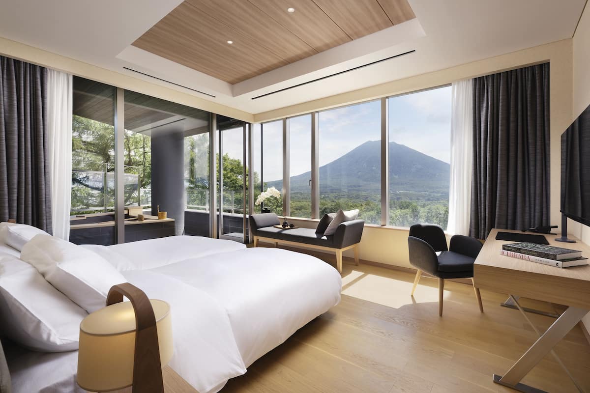 A modern hotel room with a large bed, a desk, and a view of a mountain.