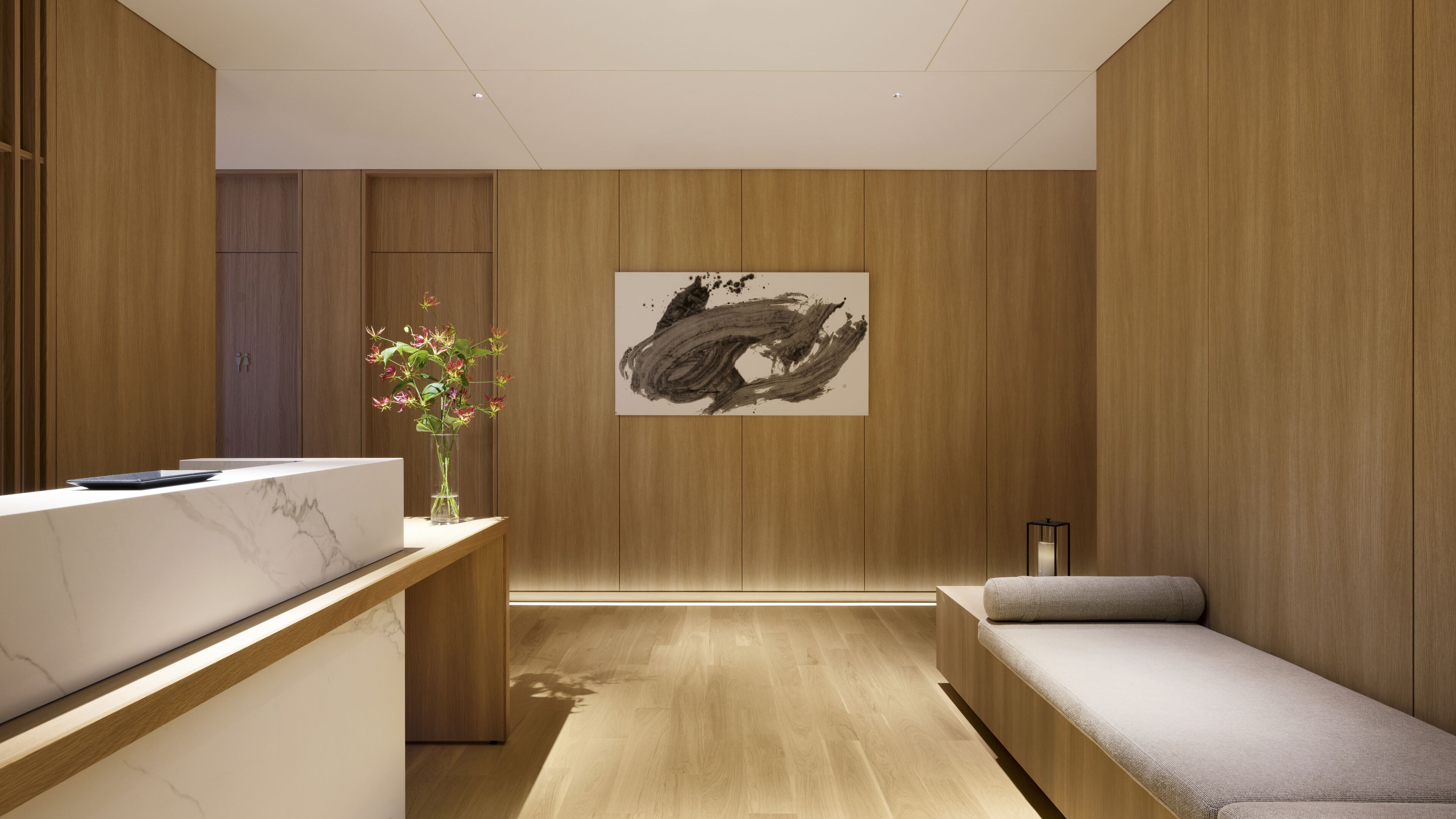 A modern spa room with wooden paneling, a reception desk, a massage table, and a painting on the wall.