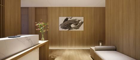 A modern spa room with wooden paneling, a reception desk, a massage table, and a painting on the wall.