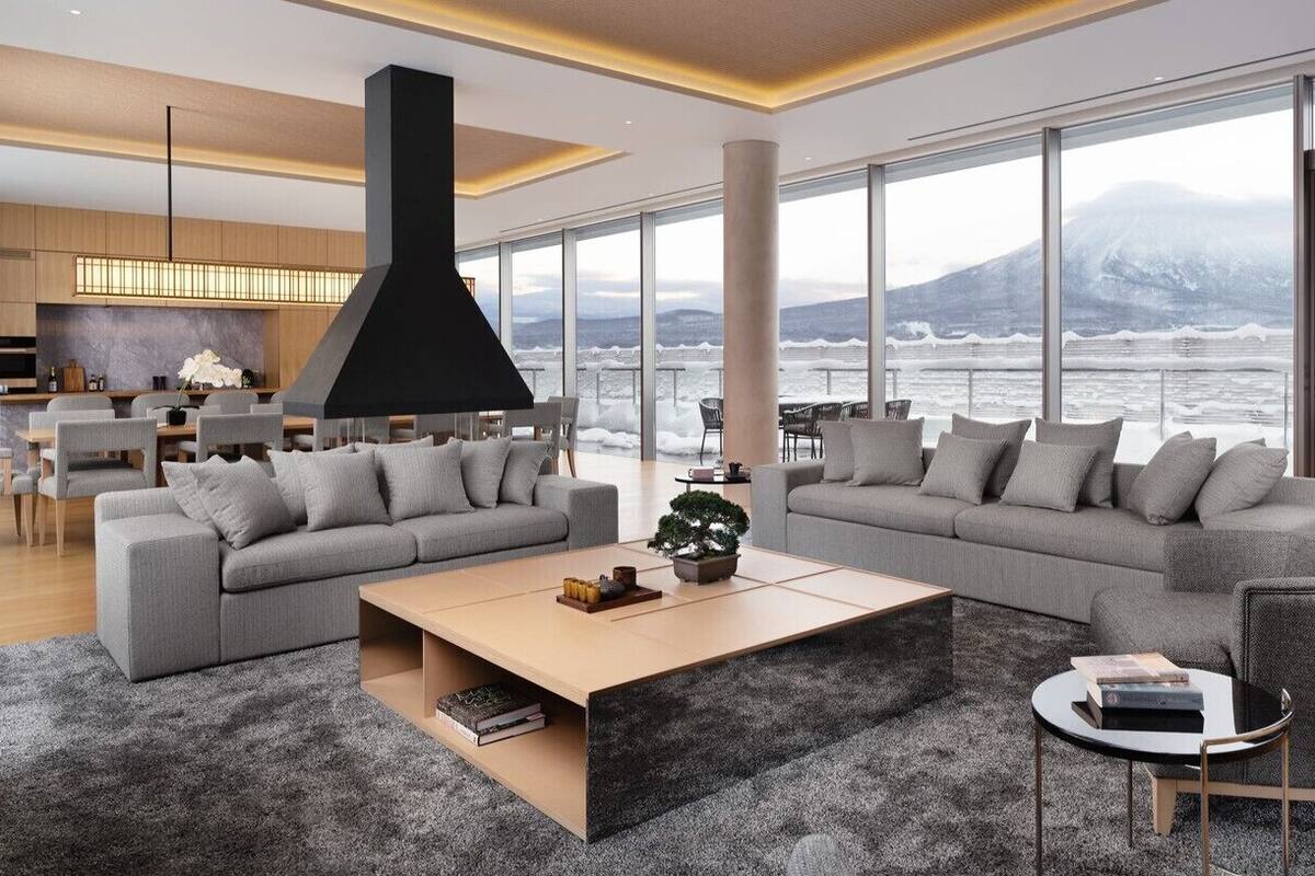 A modern living room with a large sofa, a coffee table, and a view of a snowy mountain and water.
