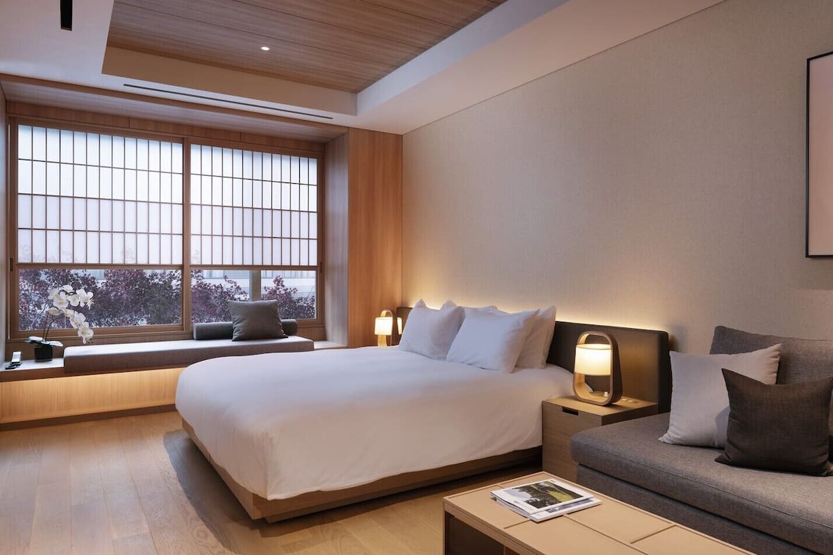 Una camera d'albergo con un letto, un divano, un comodino, una finestra con vista e un quadro appeso al muro.
