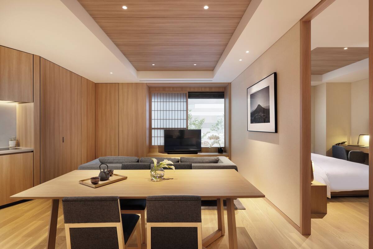 A modern hotel room with a wooden ceiling, a dining area with a table and chairs, a sofa, a TV, and a bed.