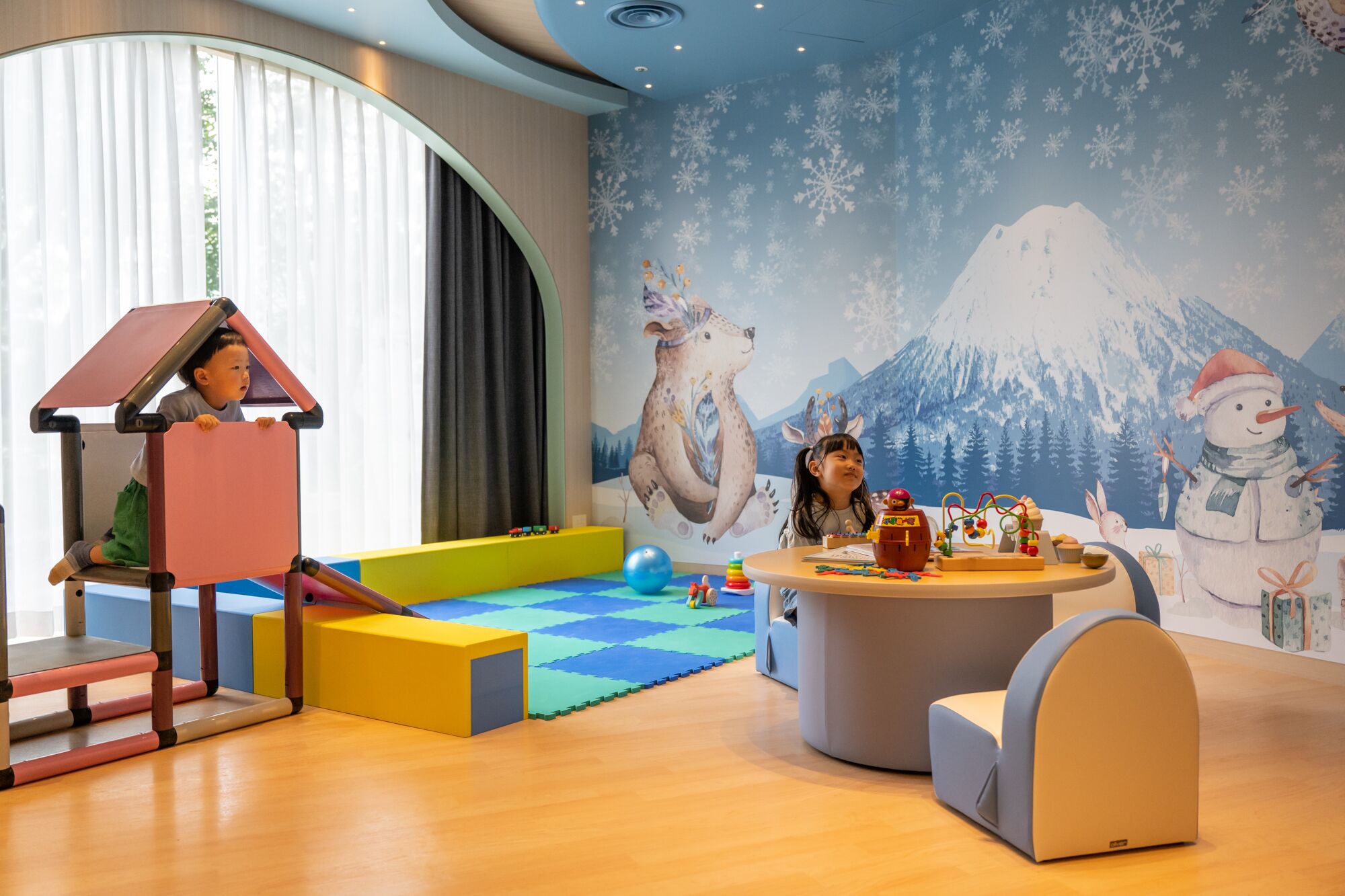 A play area with a climbing structure, a play mat, and a wall mural with a snowy mountain scene.