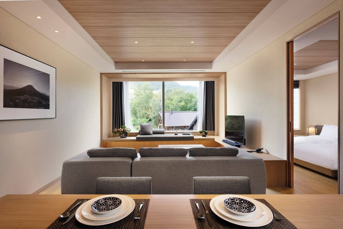 A modern hotel room with a sofa, dining table, and a bed.