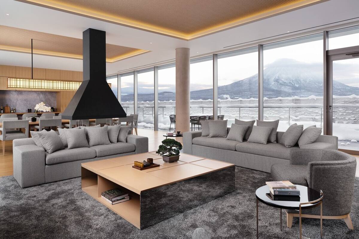 A modern living room with a large sofa, a coffee table, and a view of a snowy landscape through large windows.