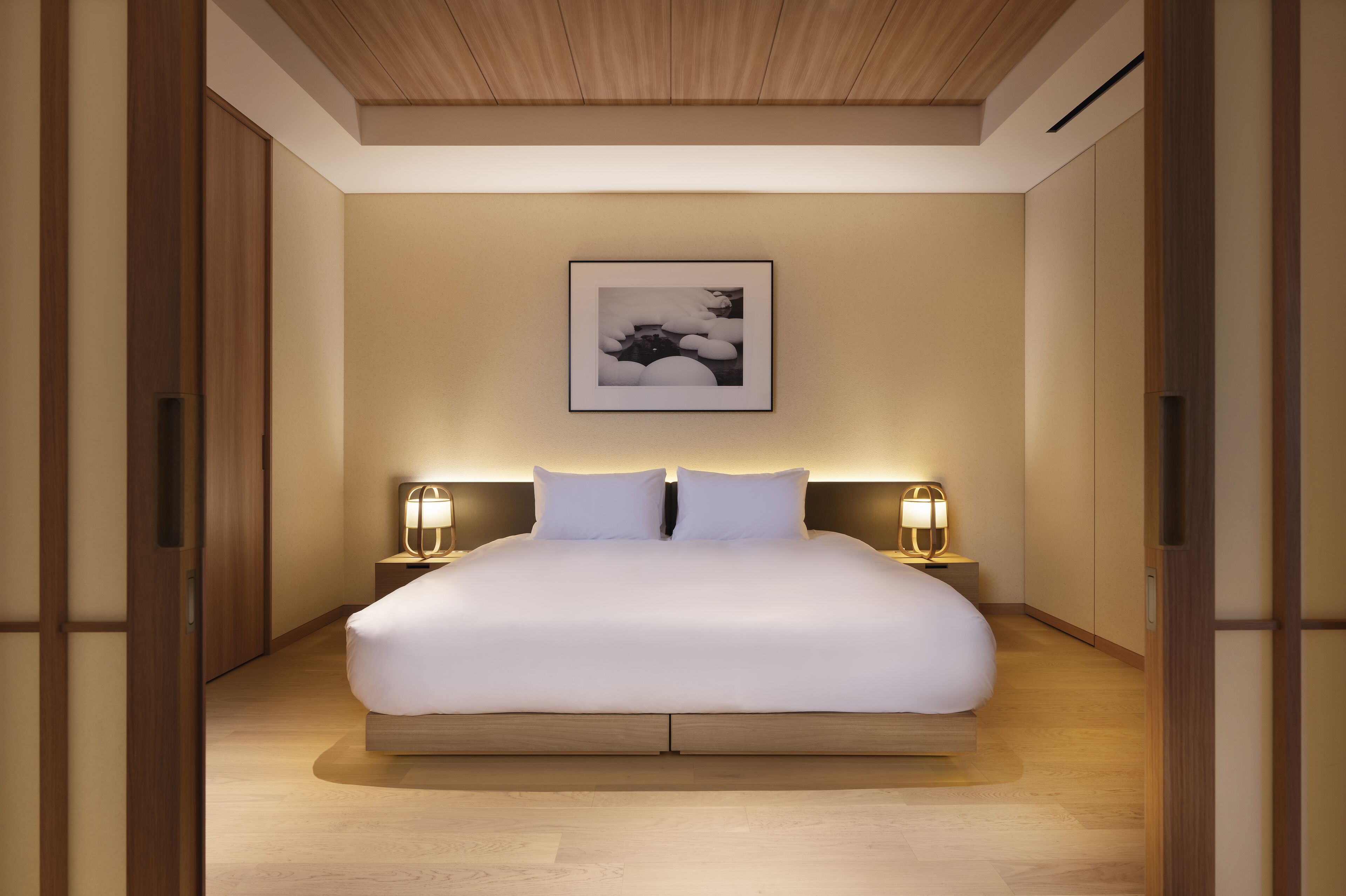 A spacious bedroom with a large bed, wooden flooring, and a framed artwork above the bed.