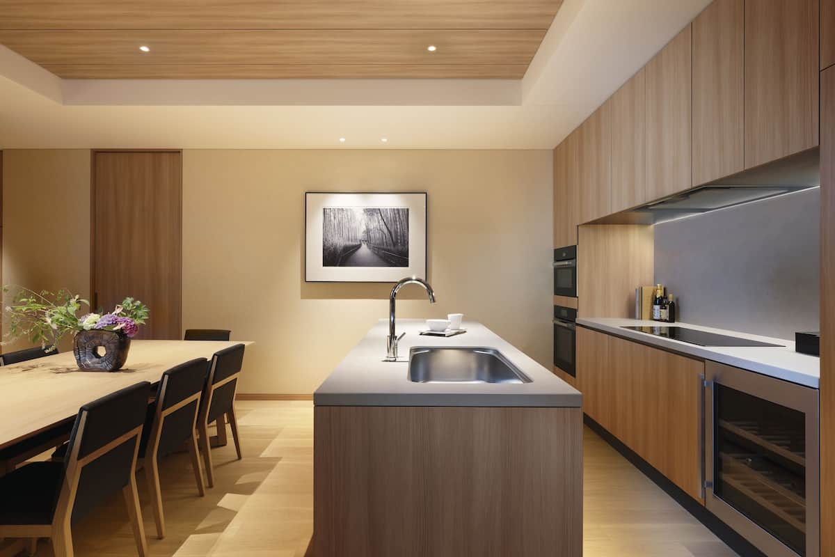 A modern kitchen with wooden cabinets, a central island with a sink, and a dining area with chairs and a table.