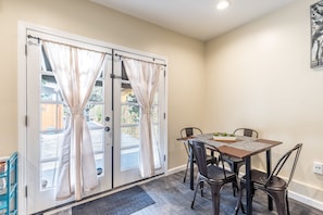 A dining area with a table and chairs, a window with curtains, and a door with a view of the outside.