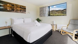 Habitación de hotel con una cama grande, una silla, una mesita y ventana con vistas a la montaña.