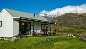 Una casa moderna con un amplio ventanal, techo verde y vistas a montañas nevadas al fondo.