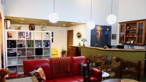 A cozy living room with a red leather sofa, a bookshelf, and a kitchen area with a stone wall and wooden cabinets. - Vineyard Accomodation - Self Catering (Henty)