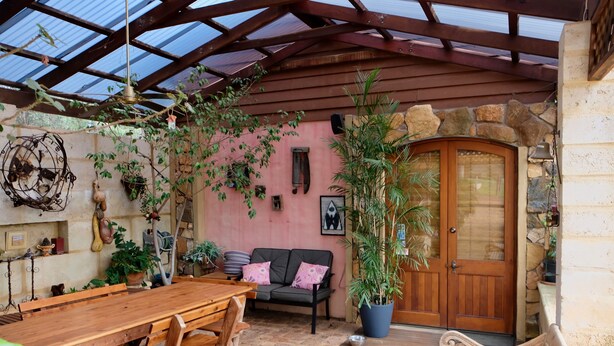 A covered patio with a wooden table and benches, a stone wall, and a wooden door. - Vineyard Accomodation - Self Catering (Henty)
