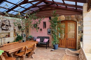 A covered patio with a wooden table and benches, a stone wall, and a wooden door. - Vineyard Accomodation - Self Catering (Henty)